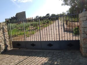portón de herreria para entrada de finca con puntas de lanza de seguridad. macollones ornamentales y zócalo con medallones decorativos.